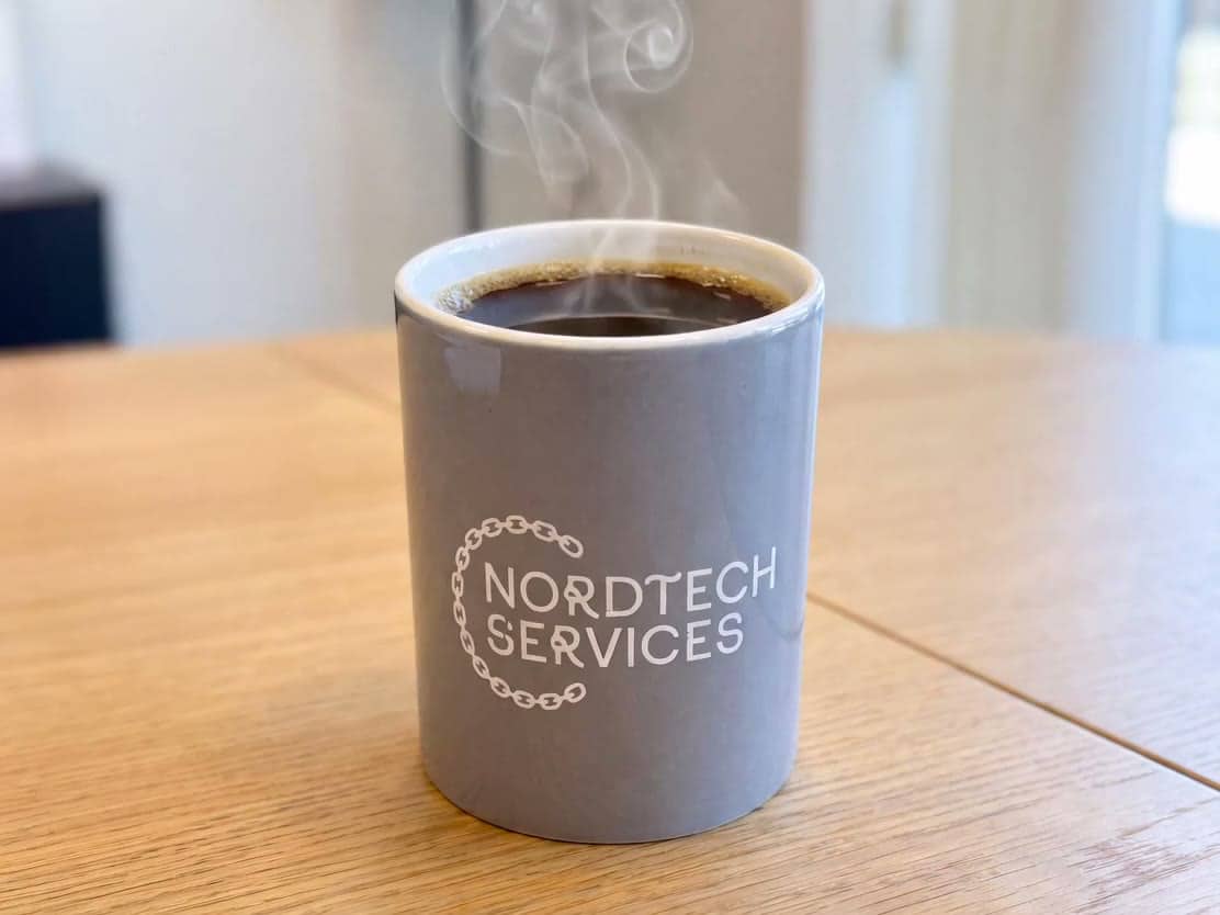 Dampende kaffekopp med Nordtech Services-logo på bordet i kontormiljøet