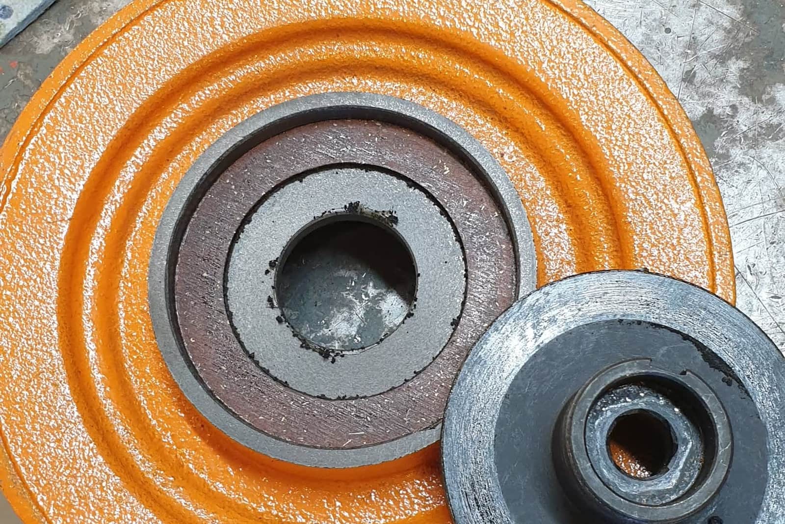 Oransje bremseskive, lagre og deler til en kjettingtalje ligger utover arbeidsbenken